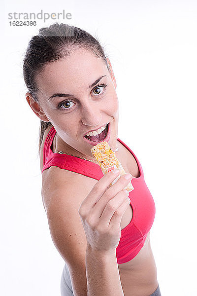 Fröhliche junge kaukasische Frau isst Diät-Müsliriegel.
