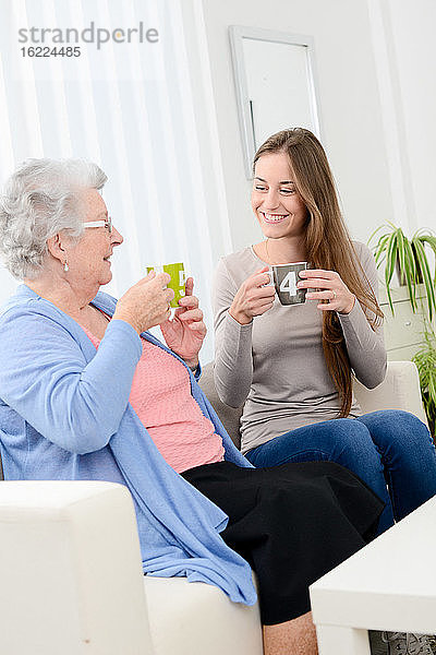 Glückliche alte ältere Frau  die mit einem fröhlichen jungen Mädchen zu Hause Tee trinkt