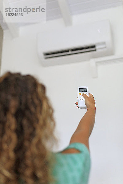 Junge Frau  die eine Fernbedienung für eine an der Wand montierte Klimaanlage benutzt.