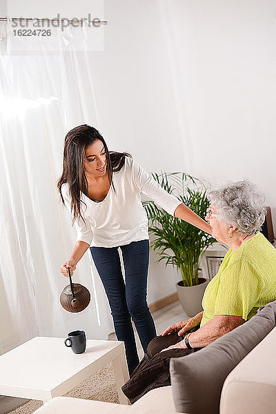Ein fröhliches junges Mädchen kümmert sich zu Hause um eine ältere Dame und serviert ihr eine Tasse Tee.