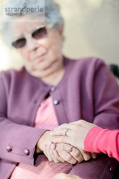 Detail der Hände einer jungen Frau  die zärtlich die Hände einer alten Seniorin halten.