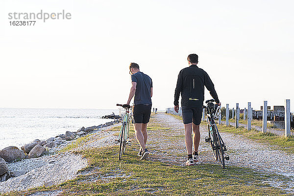 Männer zu Fuß mit Fahrrädern auf See