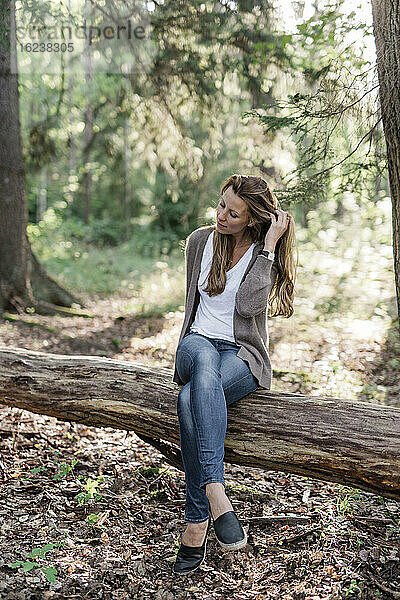 Frau sitzt auf einem Baumstamm im Wald
