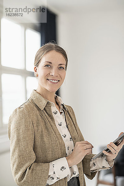 Geschäftsfrau mit Mobiltelefon schaut in die Kamera