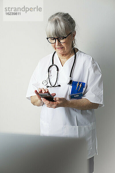 Weiblicher Arzt im Büro mit Mobiltelefon