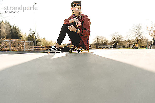 Lächelnde Frau sitzt mit ihrem Skateboard auf der Vorderseite
