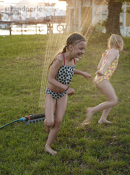 Mädchen spielen mit Wassersprinkler im Garten