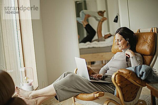 Frau sitzt auf einem Sessel und benutzt einen Laptop