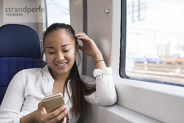 Lächelnde Frau benutzt Handy im Zug