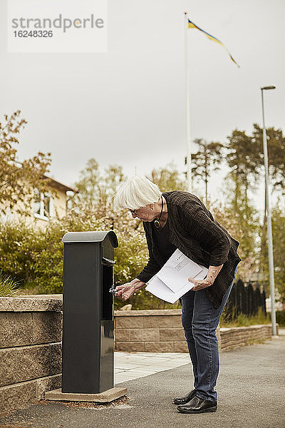 Ältere Frau steht in der Nähe des Briefkastens