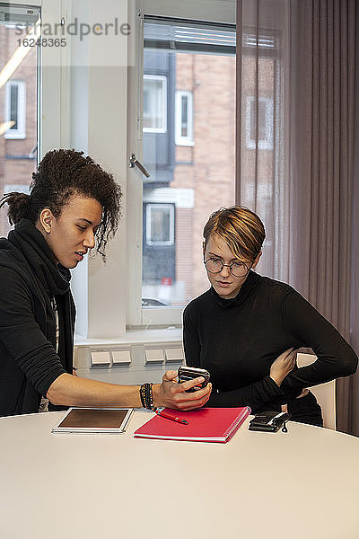 Kollegen bei der Arbeitssitzung schauen auf das Telefon