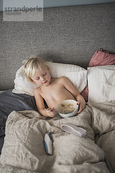 Junge im Bett und isst Müsli