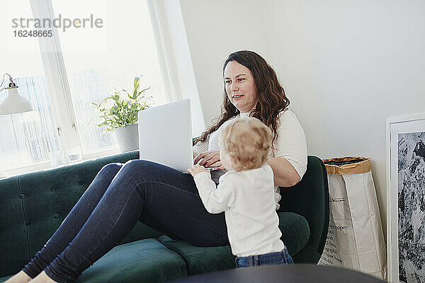Kleinkind steht in der Nähe der Mutter und benutzt einen Laptop