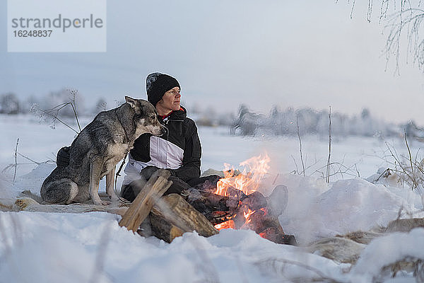 Frau mit Hund sitzt am Lagerfeuer