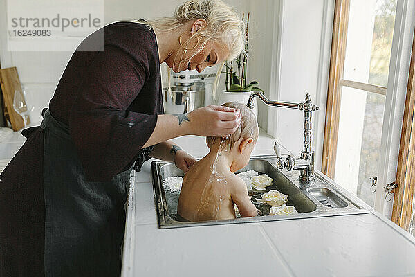 Mutter wäscht Baby in der Küchenspüle