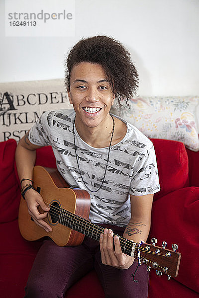 Junger Mann spielt Gitarre auf dem Sofa