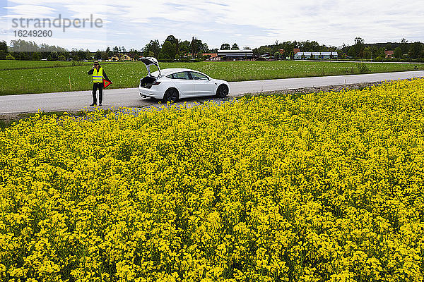 Mann am Straßenrand mit liegengebliebenem Auto