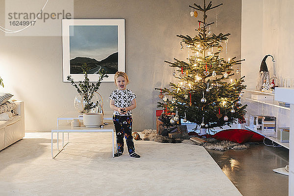 Junge steht neben Weihnachtsbaum im Wohnzimmer