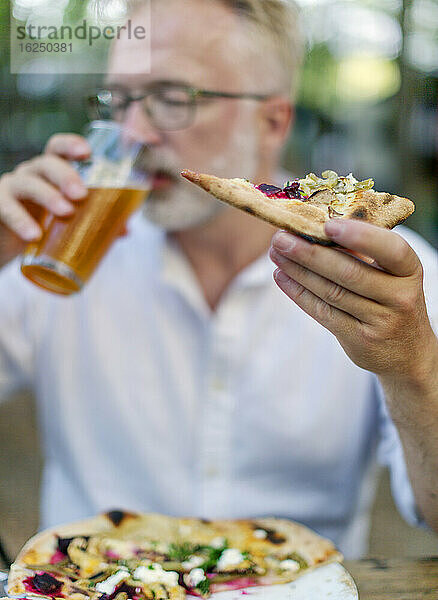 Mann isst Pizza und trinkt ein Bier