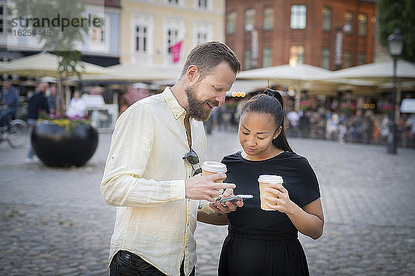 Ehepaar hält Kaffeetassen und schaut auf das Mobiltelefon