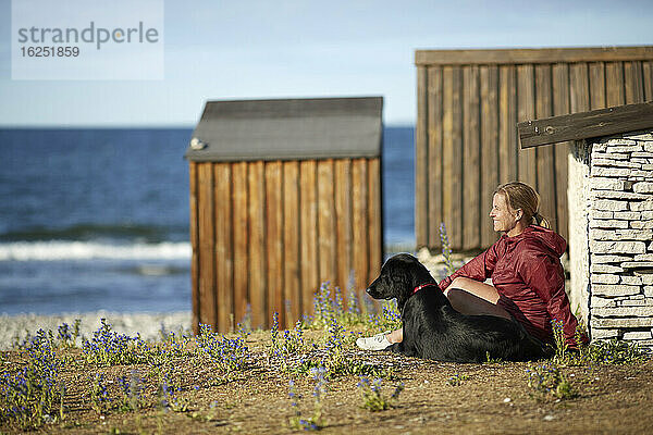 Frau mit Hund am Meer sitzend