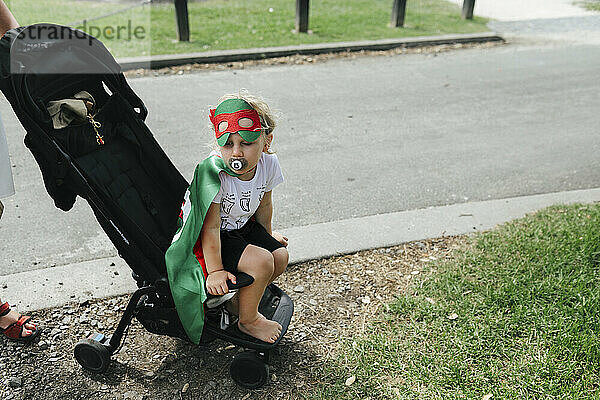 Junge im Superheldenkostüm sitzt im Kinderwagen