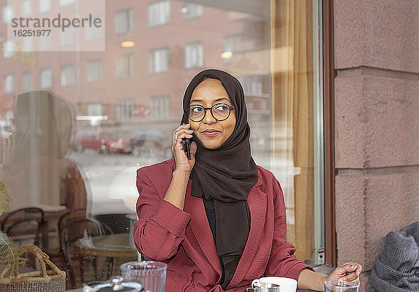 Lächelnde Frau in einem Café  die über ihr Handy spricht