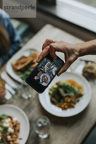 Hand mit Handy fotografiert Essen auf dem Tisch