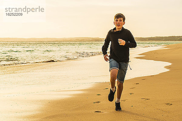 Junge läuft am Strand bei Sonnenuntergang