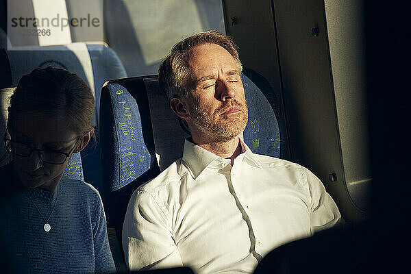 Mann sitzt mit geschlossenen Augen im Zug