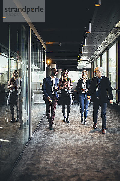 Lächelnde Unternehmerinnen und Unternehmer beim Gang durch den Bürokorridor