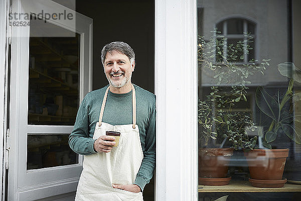 Porträt eines selbstbewussten reifen männlichen Besitzers beim Kaffee trinken am Eingang des Kunstateliers