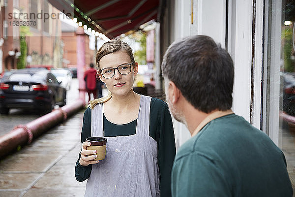 Selbstbewusste Frau trinkt Kaffee mit einem männlichen Mitarbeiter vor dem Kunstatelier