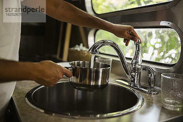 Mittelsektion eines Mannes  der Wasser durch den Wasserhahn im Wohnwagen füllt