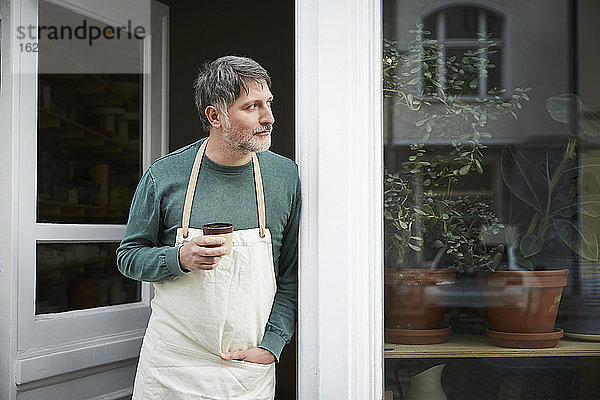 Reifer männlicher Besitzer schaut beim Kaffee trinken am Eingang des Kunstateliers weg