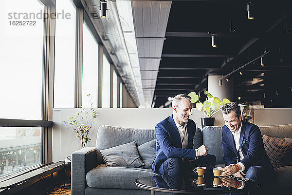 Fröhliche Unternehmer diskutieren mit Tee  während sie im Büro sitzen