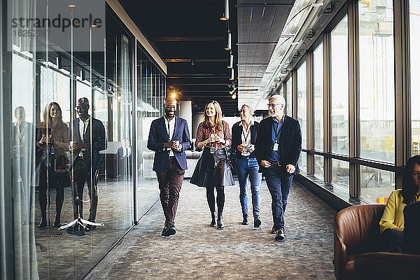 Lächelnde weibliche und männliche Kollegen gehen am Arbeitsplatz im Korridor