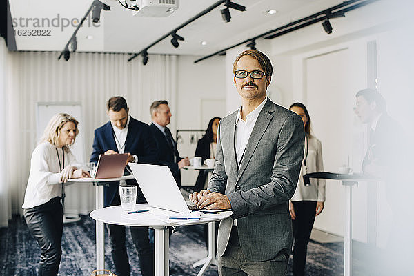 Portrait eines Geschäftsmannes  der über einen Laptop arbeitet  während er im Büro steht Seminar