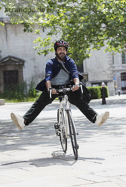 Verspielter Geschäftsmann beim Fahrradfahren auf dem sonnigen Bürgersteig der Stadt