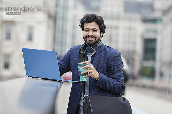 Porträt eines lächelnden Geschäftsmannes mit Laptop und Kaffee auf der Stadtbrücke