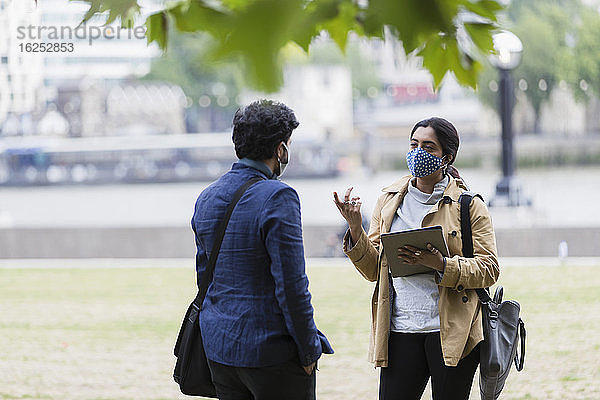 Geschäftsleute mit Gesichtsmasken und digitalem Tablet-Gespräch im Stadtpark