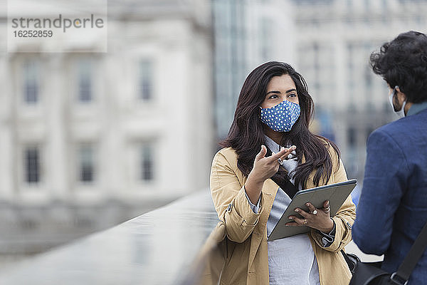 Geschäftsleute mit Gesichtsmasken mit digitalem Tablet  die im Freien sprechen