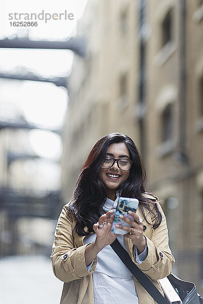 Lächelnde Frau mit Smartphone auf dem Bürgersteig