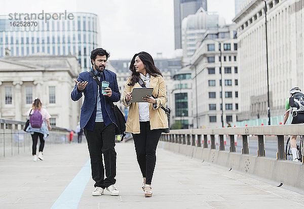 Geschäftsleute mit Kaffee und digitalem Tablet im Gespräch auf der Stadtbrücke