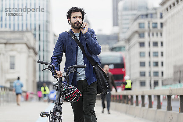 Geschäftsmann mit Fahrrad spricht mit Smartphone auf der Stadtbrücke