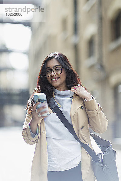 Lächelnde Geschäftsfrau benutzt Smartphone auf der Straße