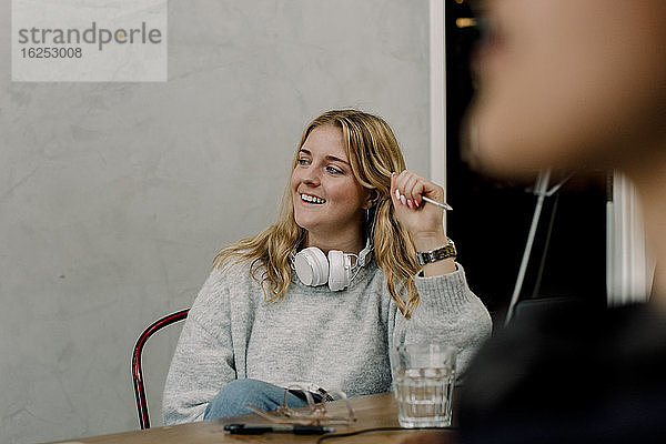 Lächelnde Geschäftsfrau mit Kopfhörern am Arbeitsplatz sitzend