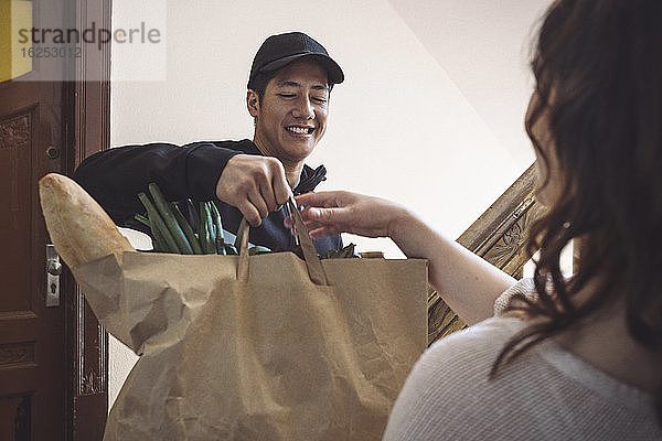 Lächelnder Lieferant liefert Gemüse an Kunden aus  während er vor der Tür spricht