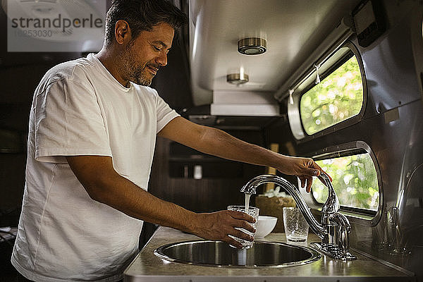 Lächelnder Mann füllt Trinkwasser durch Wasserhahn im Wohnwagen