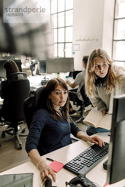 Weibliche Mitarbeiterin benutzt Computer  während der Unternehmer im Büro diskutiert